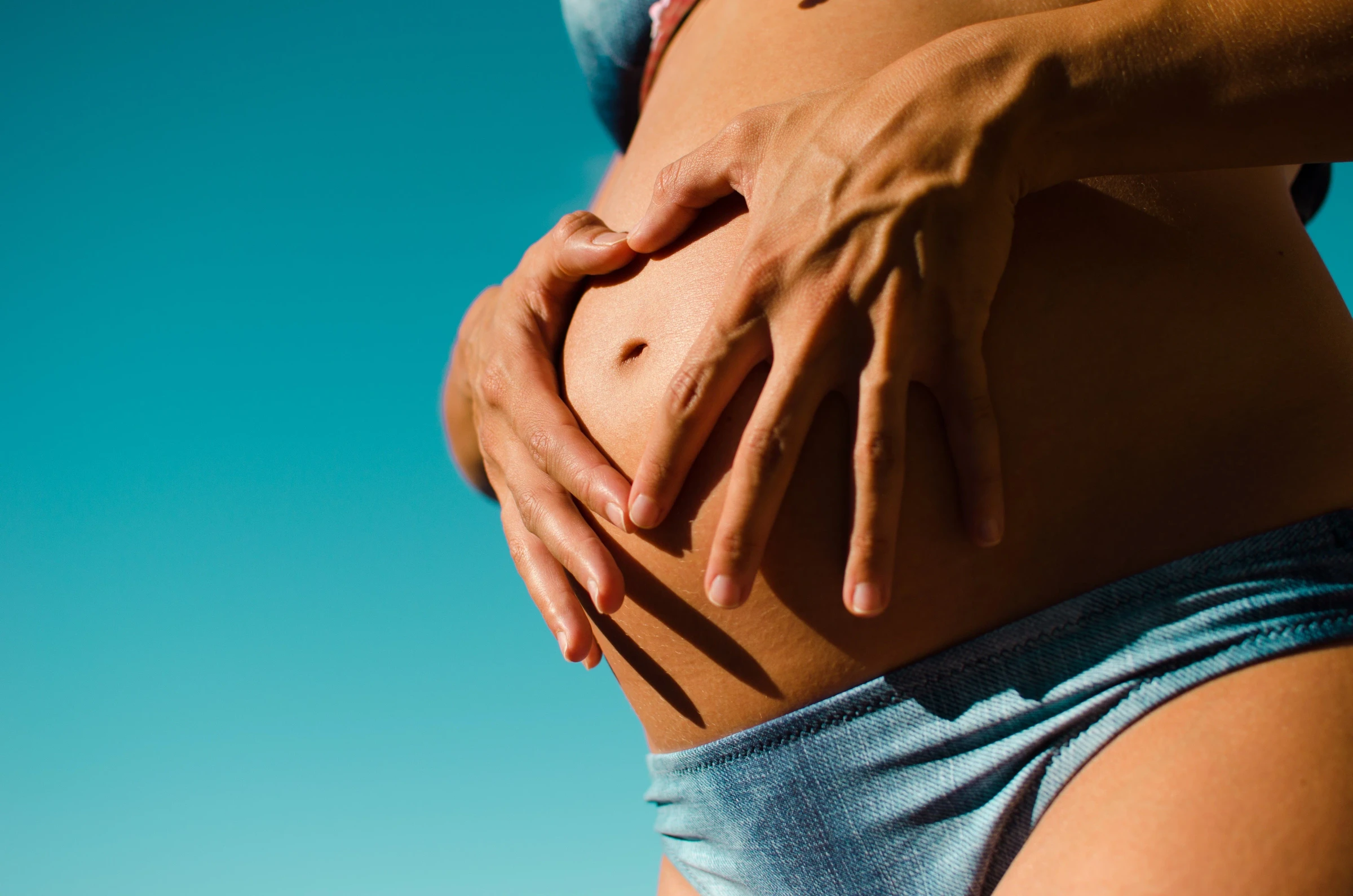 Hands resting on a pregnant belly against a teal background
